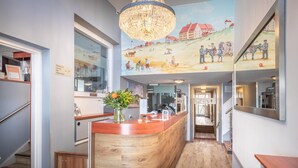 A reception area with a wooden counter, a chandelier, and a mural depicting a historical scene. - Hotel Astoria (Noordwijk)