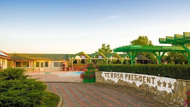 Entrada de hotel con pared de piedra, un letrero que dice 'TERRASA PRESIDENT' y un área exterior cubierta con vegetación.