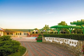 A hotel entrance with a stone wall, a sign reading 'TERRASA PRESIDENT', and a covered outdoor area with greenery.