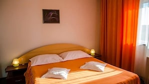 Una habitación de hotel con una cama, dos lámparas de noche, un cuadro en la pared y cortinas anaranjadas.