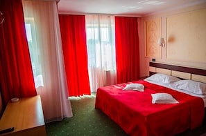 A hotel room with a bed, a bedside table, a lamp, and a window with curtains.