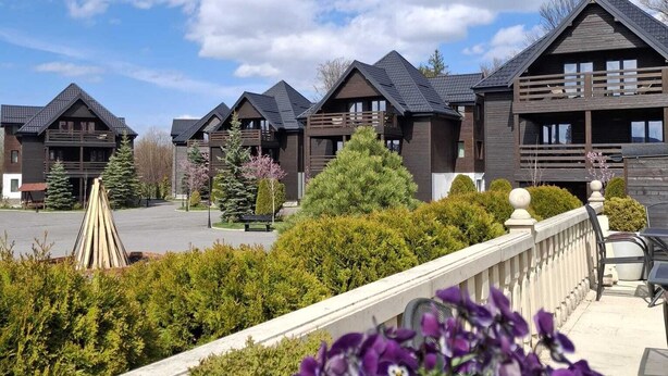 A row of modern, dark-colored cabins with a balcony, surrounded by greenery and a clear sky. - Monterai Resort (Brasov)