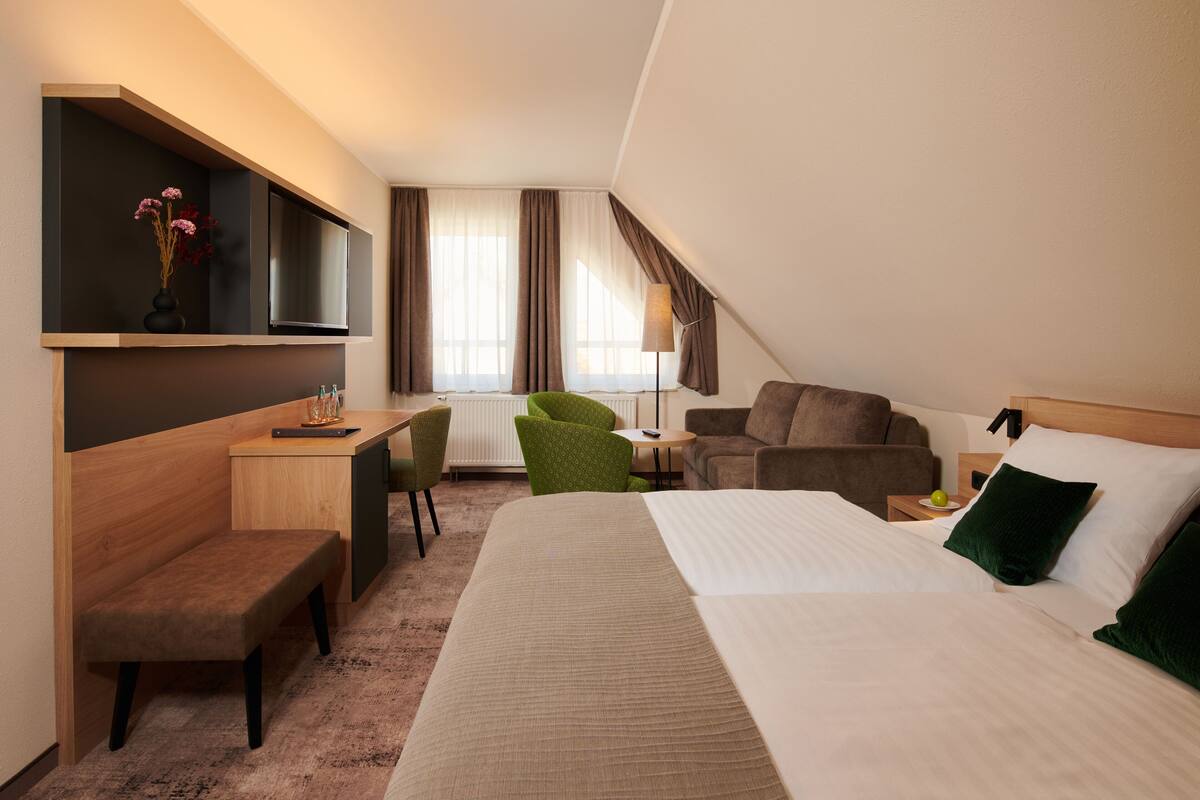 Une chambre d’hôtel équipée d’un lit, d’un bureau, d’une chaise, d’un canapé, d’une télévision et d’une fenêtre avec des rideaux.