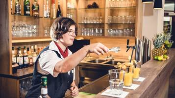Un barman preparando bebidas en una barra, con estantes llenos de botellas y vasos al fondo.