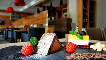 Un postre con fresas y hojas de menta sobre un plato de pizarra, con un fondo desenfocado del interior de un restaurante.