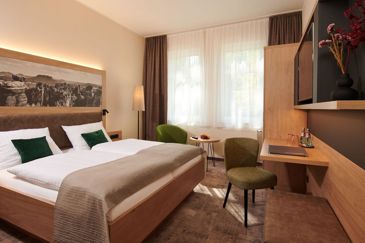 Une chambre d’hôtel avec un grand lit, un bureau avec une chaise, une petite table et une fenêtre avec des rideaux.