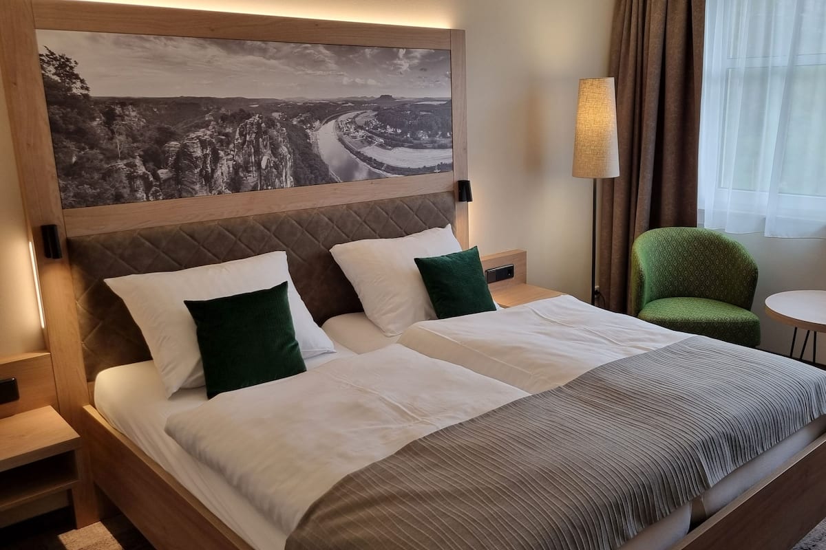 Une chambre d’hôtel avec un lit, une chaise verte, une petite table et un tableau au mur.