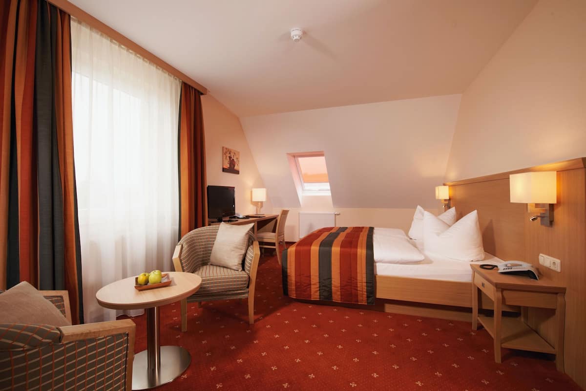 Une chambre d’hôtel avec un lit, un bureau, une chaise, une petite table avec des pommes et un téléviseur.