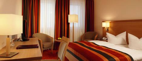 Una habitación de hotel con cama, escritorio, silla, lámpara y mesita de noche.