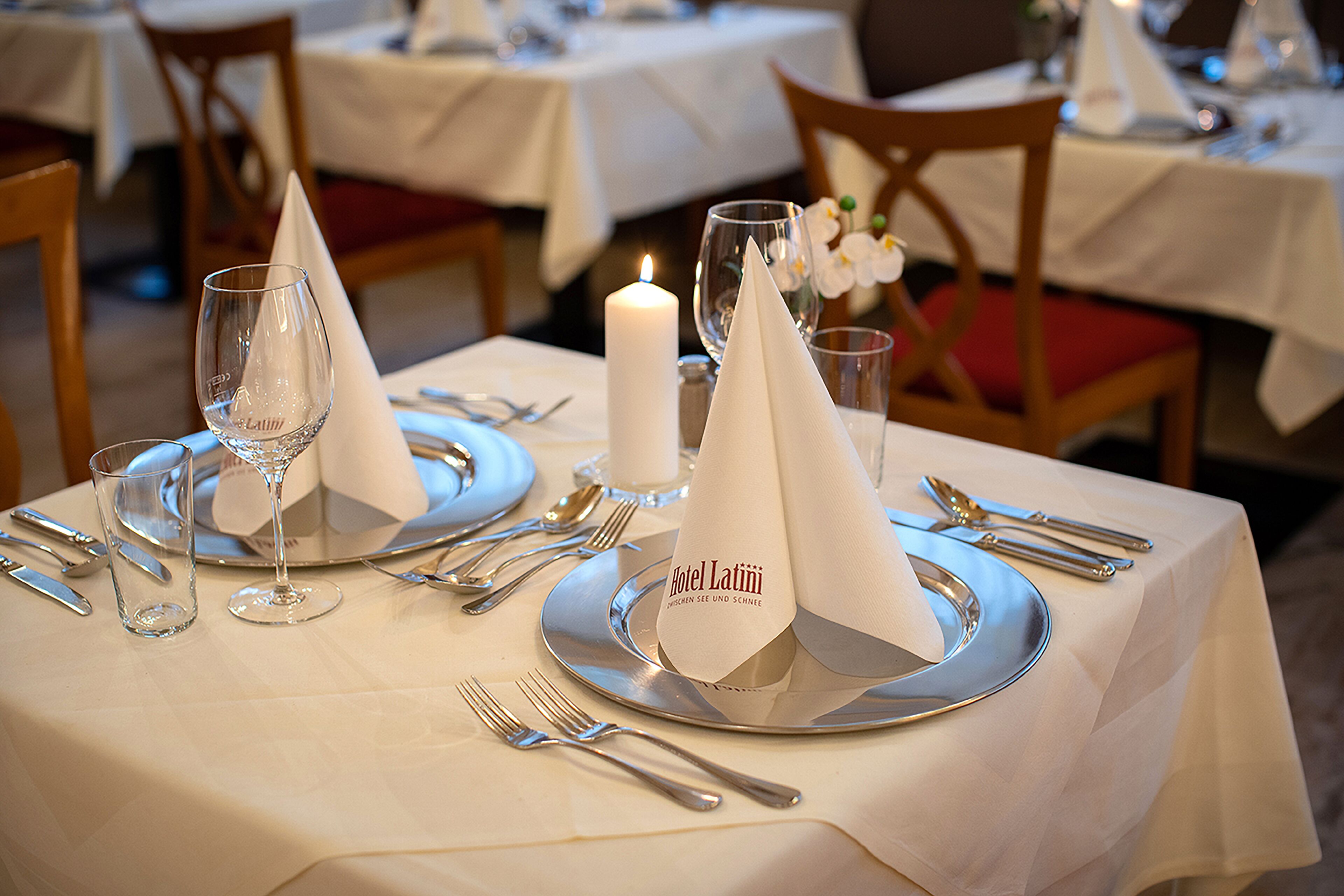 A table set for a meal with a lit candle, a glass of water, and a napkin with the hotel name.