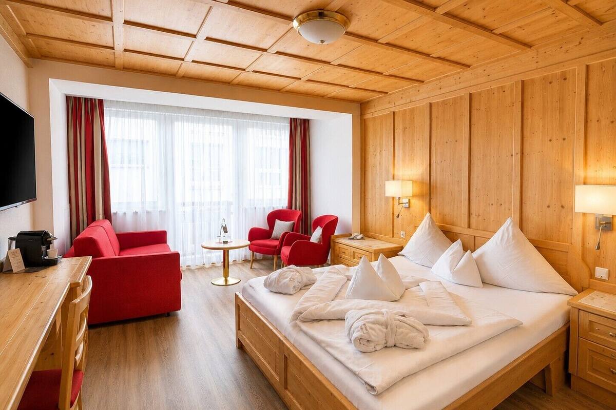 A hotel room with a wooden ceiling, a bed with white linens, a red sofa, a small table, and a TV.