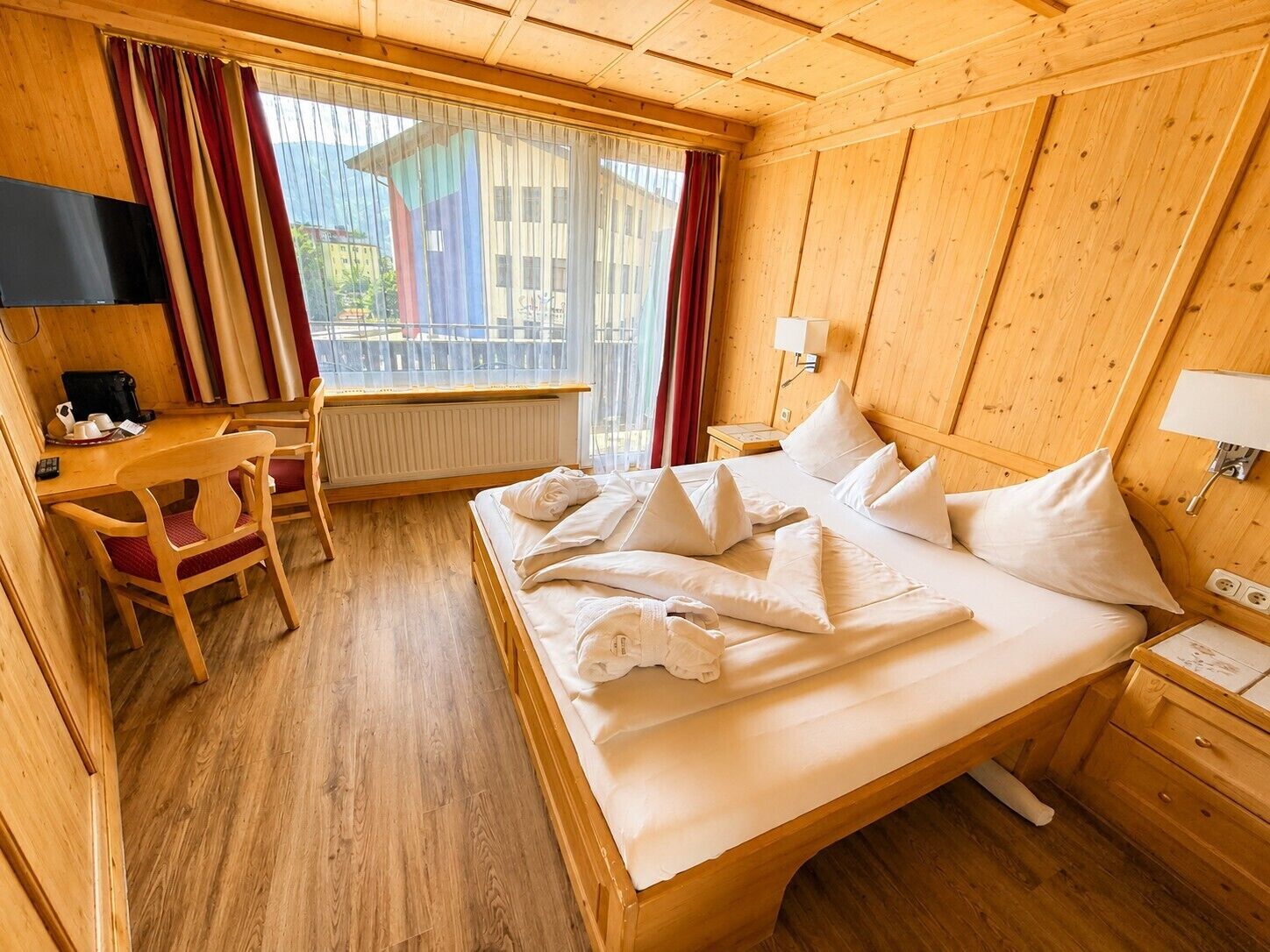 A wooden room with a bed, a desk, and a window.