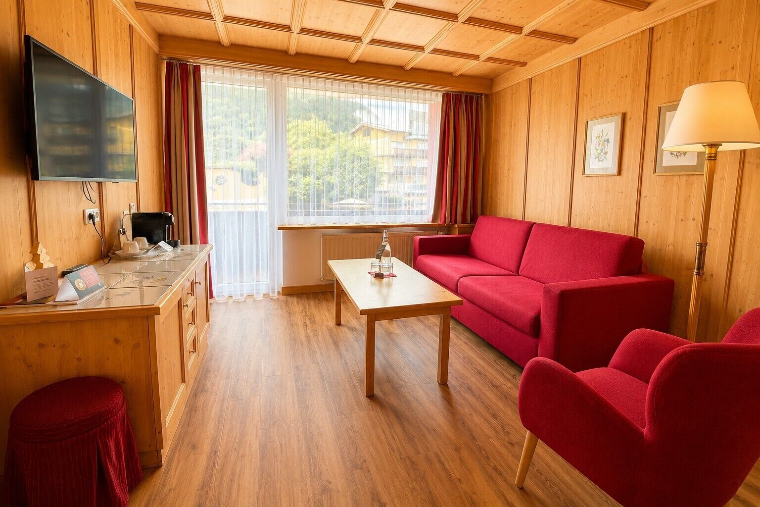 A room with a wooden interior, a sofa, a table, a TV, and a window with curtains.