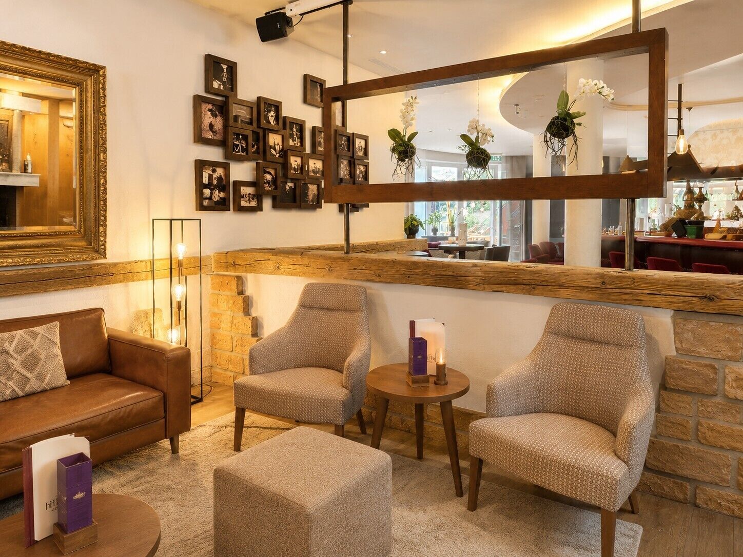Un espacio de sala cálido y acogedor con un sofá de cuero marrón, dos sillones estampados, una mesita redonda y un espejo grande que refleja la habitación.