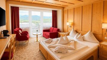 A hotel room with a bed, two red armchairs, a small round table, a desk with a coffee maker, and a TV.