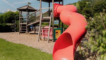 A playground with a red slide, a wooden playhouse, and a staircase.