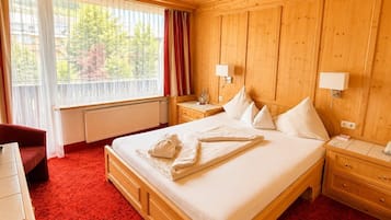 A hotel room with a wooden bed, two bedside tables, a red carpet, a window with curtains, and a view of trees.