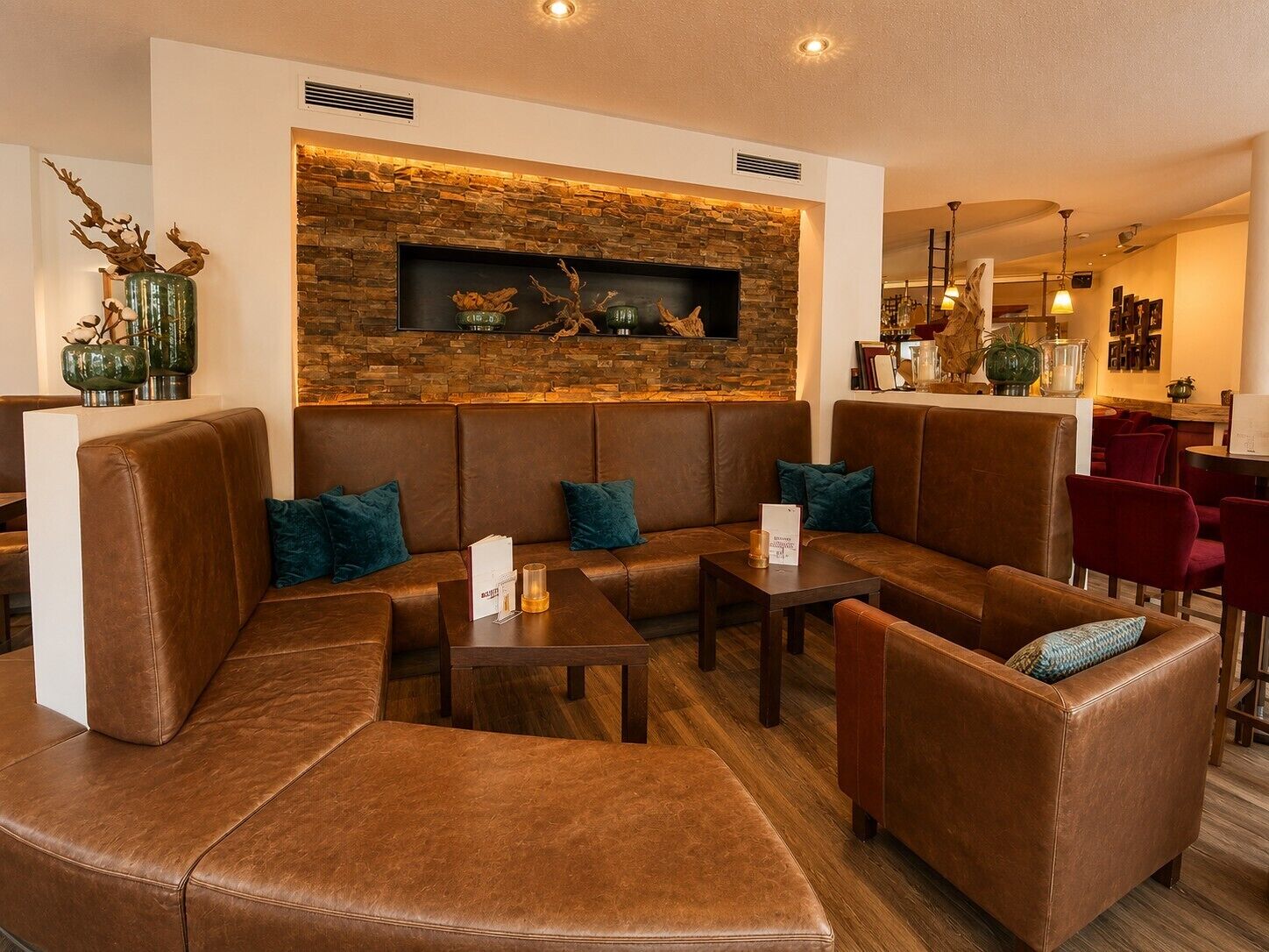 Ein stilvoller Lounge-Bereich mit Ledersitzgelegenheiten, einer Wand aus Naturstein und einer Bar im Hintergrund.