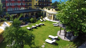 Un patio de hotel con tumbonas y zona de piscina, rodeado de vegetación exuberante y vistas a la montaña.