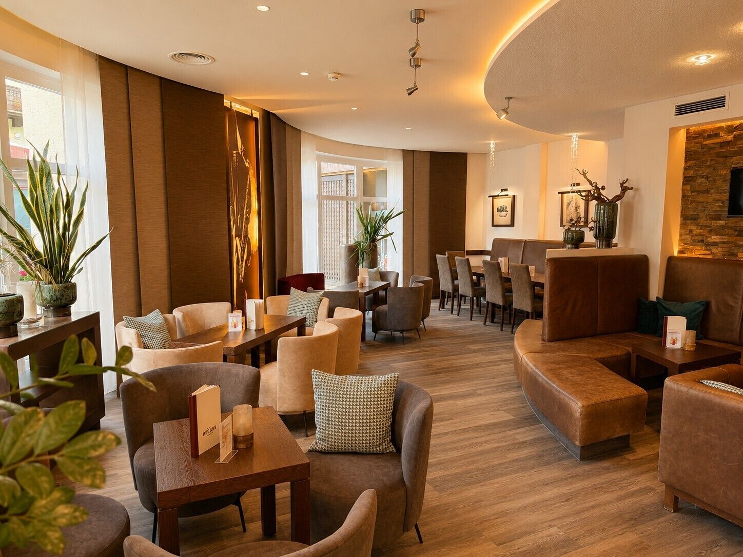 Un hall d’hôtel moderne, doté d’espaces aménagés avec des sièges, d’un comptoir d’accueil et d’un mur décoratif en pierre.