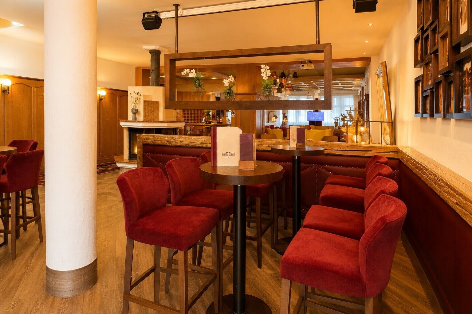 Un bar de hotel con sillas tapizadas de rojo, una barra de madera y una galería de cuadros en la pared.