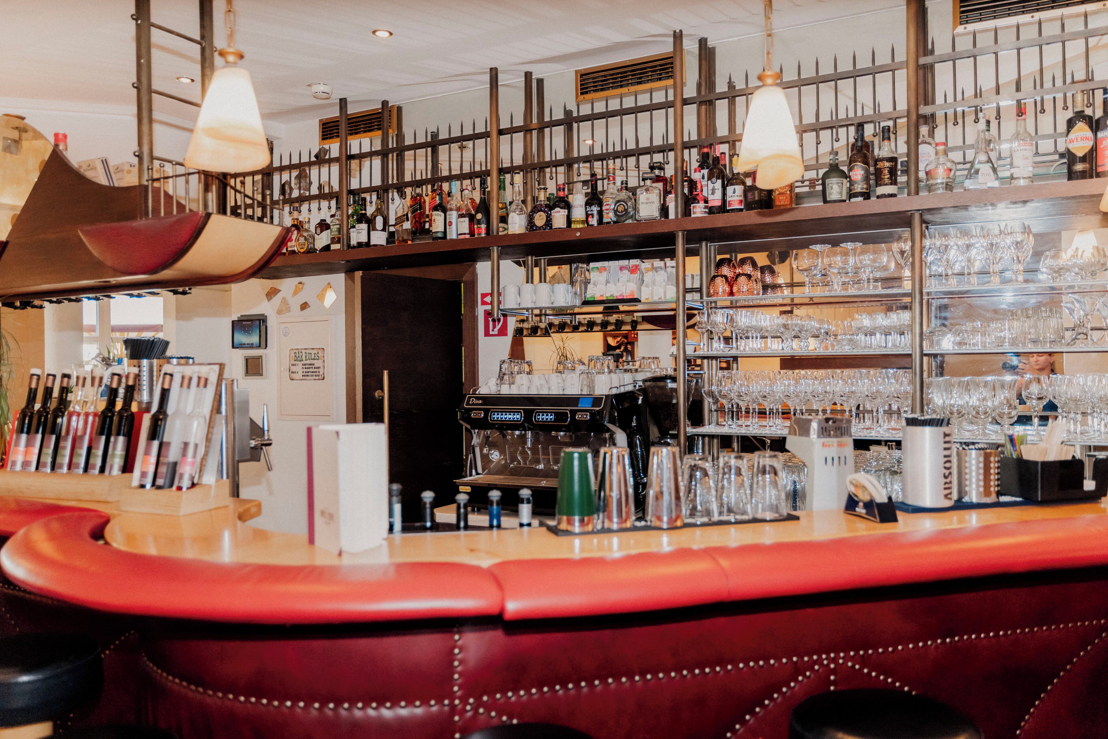 Una zona de bar con una barra curva, asientos de cuero y una variedad de botellas y vasos en estanter ías.