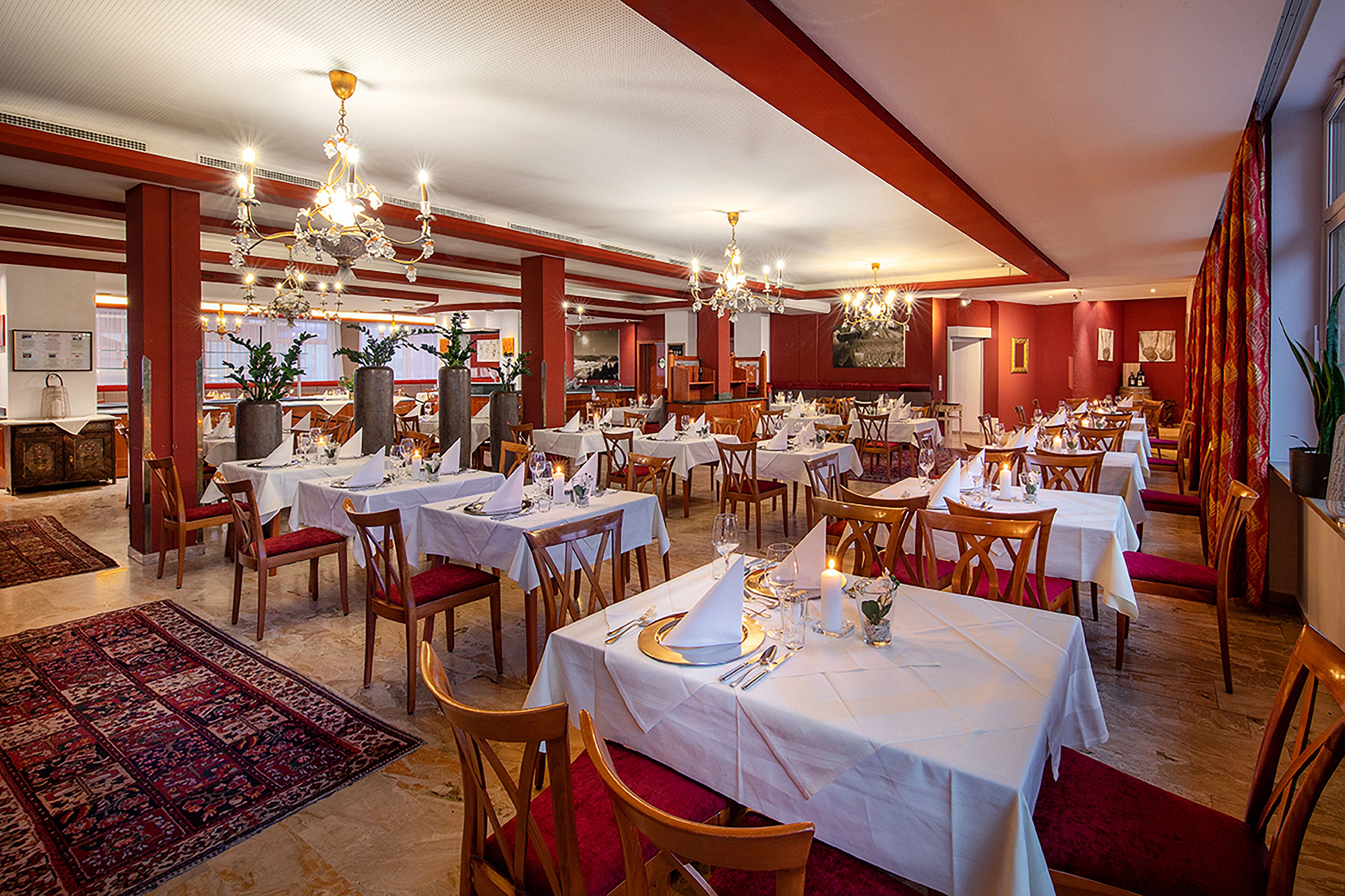 A spacious dining area with multiple tables set for dining, elegant chandeliers, and a red and white color scheme.