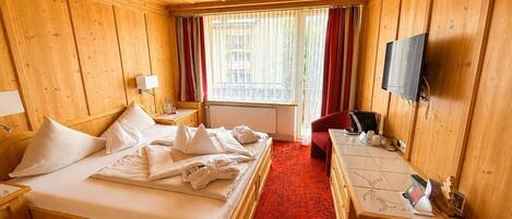 Habitación de hotel con techo de madera, una cama con sábanas blancas, un escritorio con ordenador, una silla y un televisor.