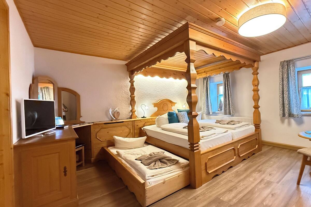 Ein Bett mit Baldachin, ein Holzfußende, ein Fernseher auf einer Holzkommode und ein kleiner Tisch mit Stuhl.