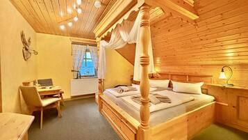 Ein hölzernes Himmelbett mit Baldachin, ein Schreibtisch mit Stuhl, eine Heizung und ein Fenster mit Vorhängen.