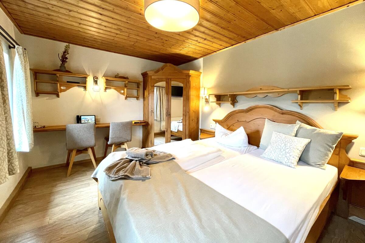 Ein Hotelzimmer mit Holzboden, einem Bett mit weißer Bettwäsche, einem Schreibtisch mit Stuhl und einem Spiegel.