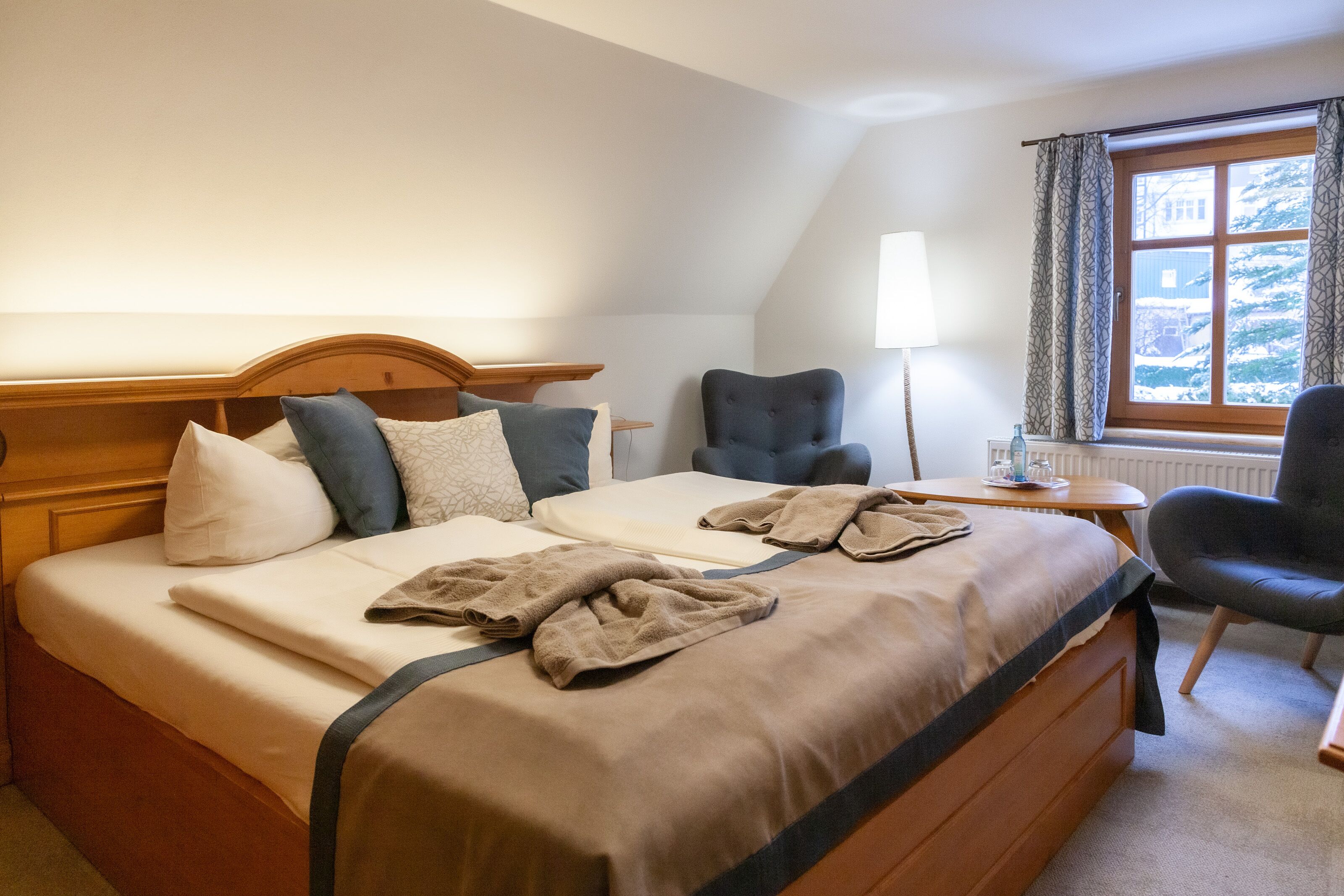 A hotel room with a bed, a chair, a table, and a window with curtains.