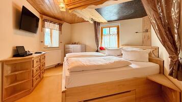 A bedroom with a bed, a desk, a TV, and a window with curtains.