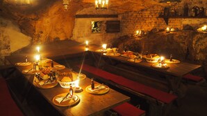 A dimly lit underground dining area with wooden tables and benches, candles, and stone walls. - Naturhotel Gasthof Bärenfels (Altenberg)