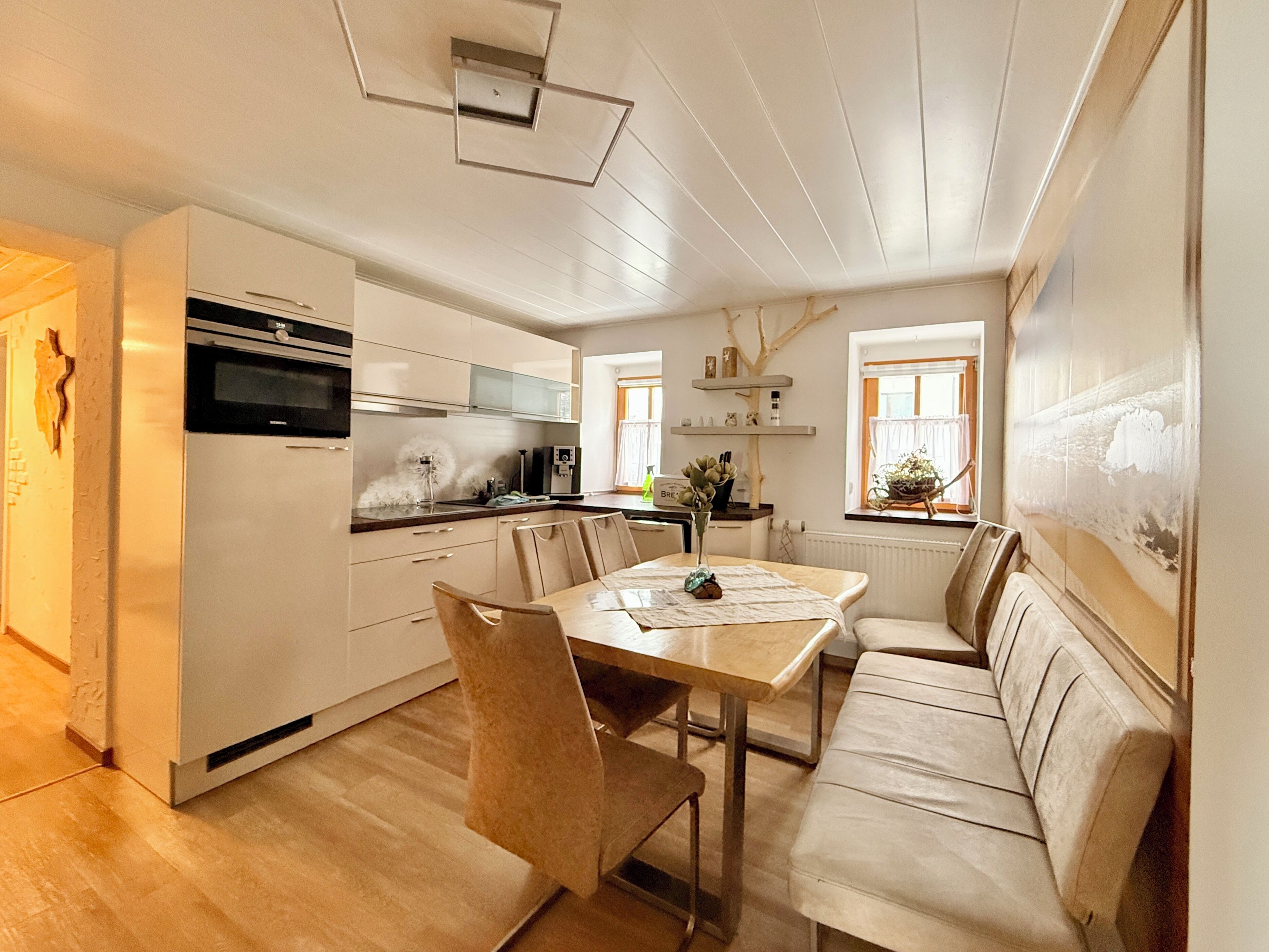 A modern kitchen with white cabinets, a dining table with chairs, a built-in oven, and a window with a view.