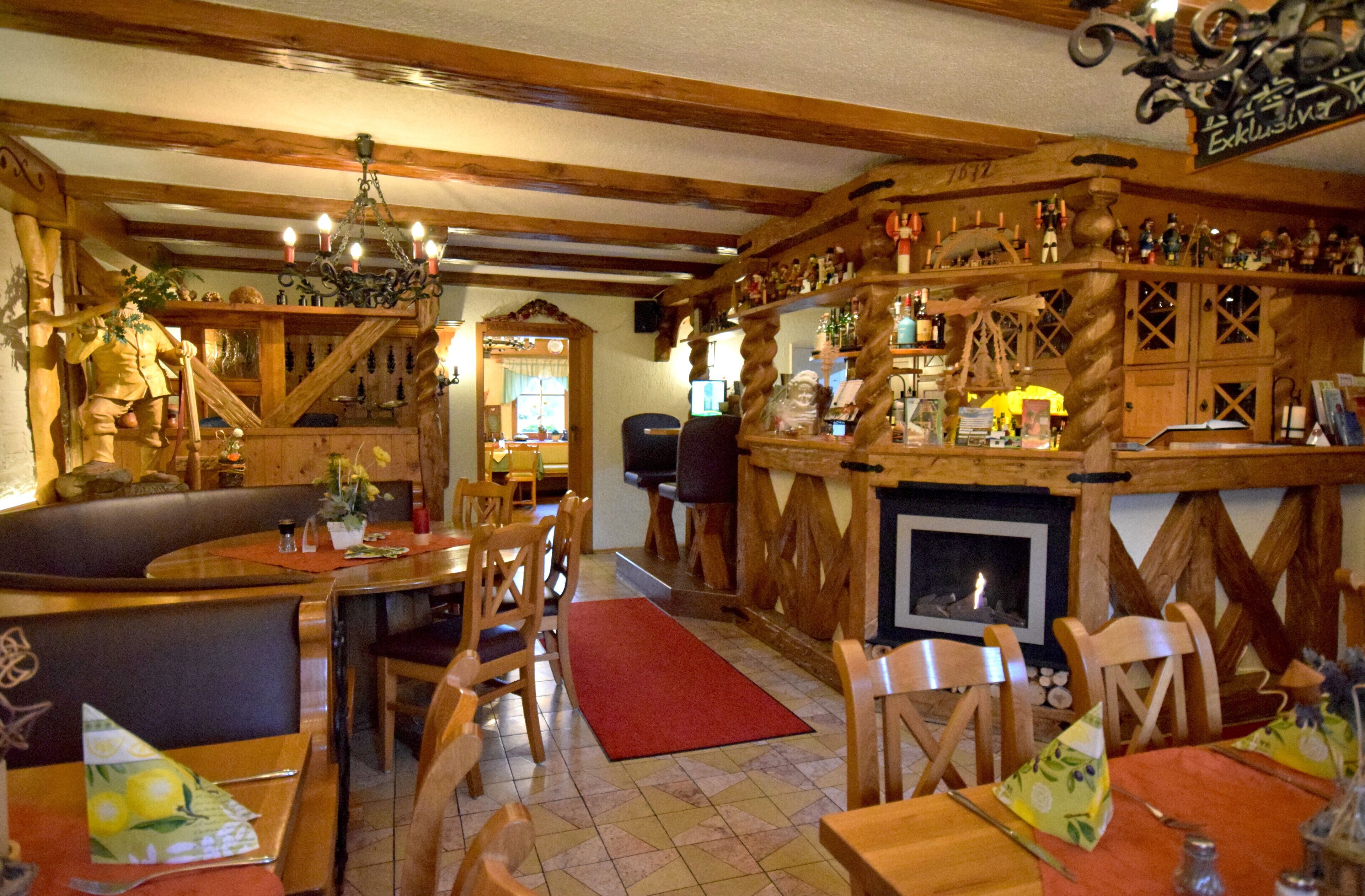 A rustic bar area with wooden beams, a fireplace, and various bottles and decorations.