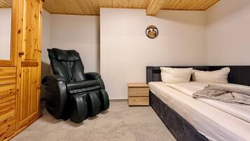 Un dormitorio con sillón de masajes, cama, armario de madera y mesita de noche.