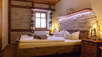 A wooden bed with white linens, a stone wall, and a window with curtains.