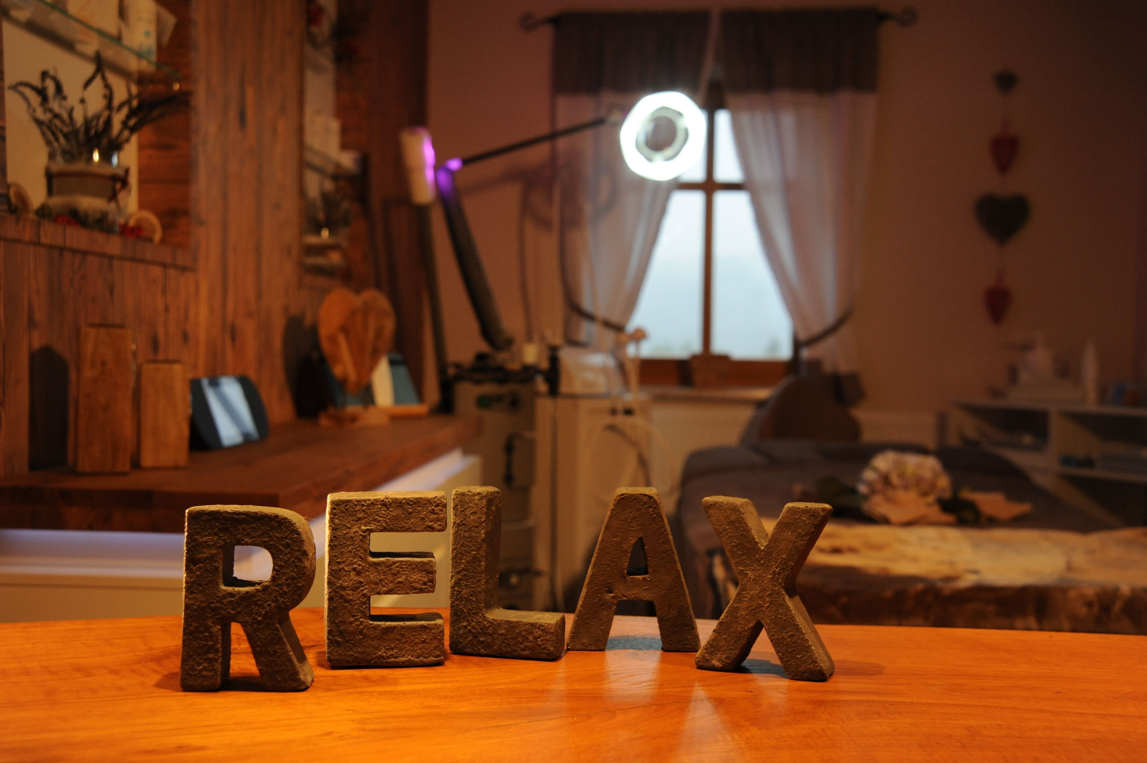A cozy room with wooden furniture, a desk with 'RELAX' spelled out on it, and a lamp in the background.