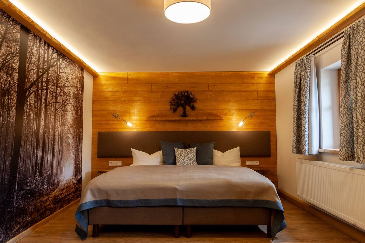 Ein modernes Schlafzimmer mit einem großen Bett, Holzwandverkleidung, einem Nachttisch und einem an der Wand befestigten Fernseher.