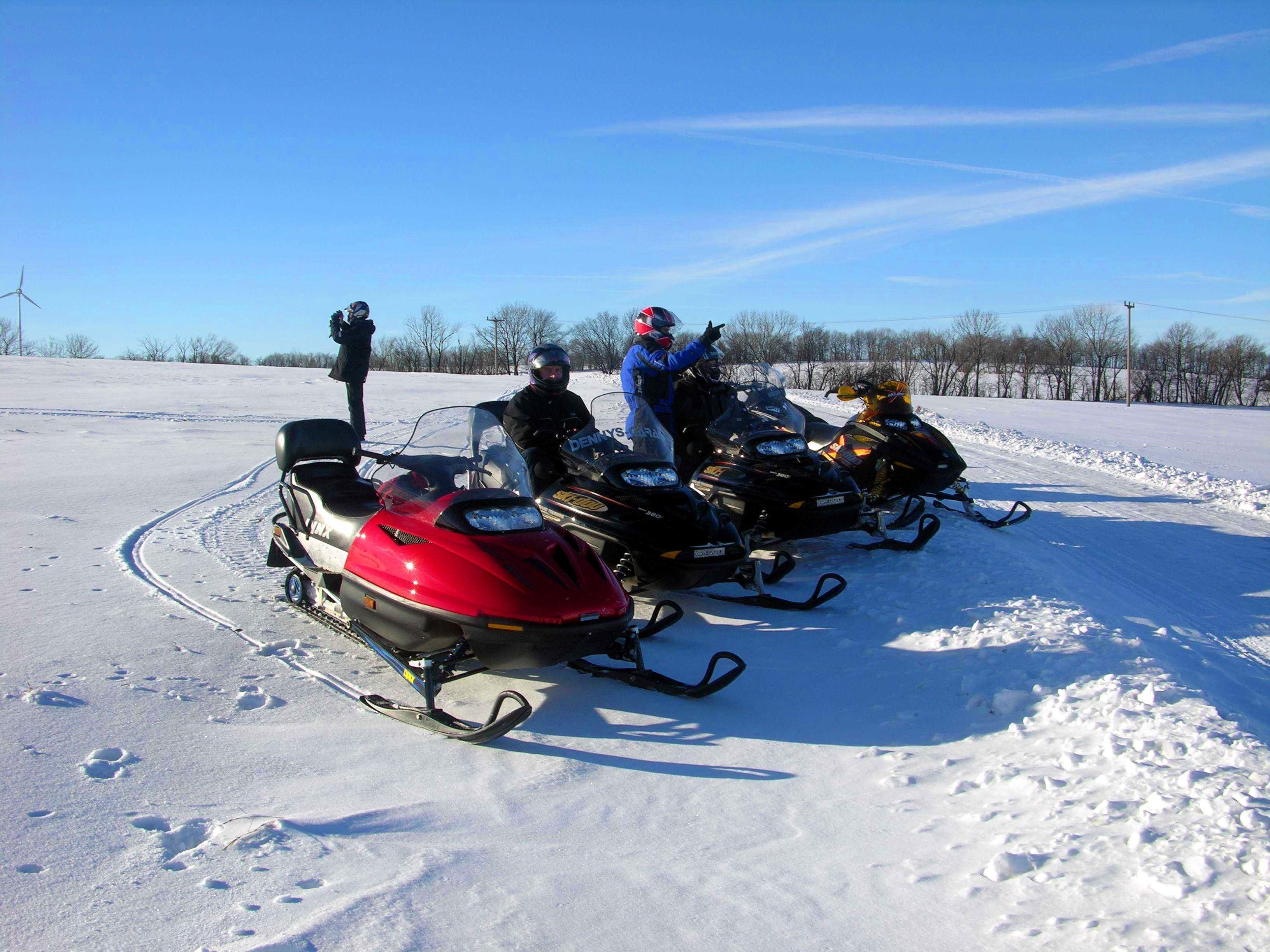A group of snowmobiles parked on a snowy field with a clear sky.