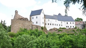 A historic building with a stone wall and white facade, surrounded by lush greenery. - Naturhotel Gasthof Bärenfels (Altenberg)