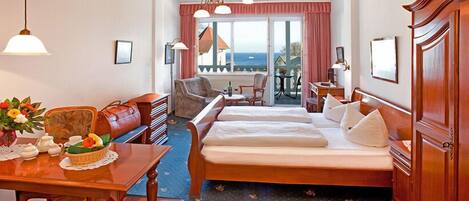A hotel room with a bed, a desk with a vase of flowers, a chair, and a view of the sea through the window.