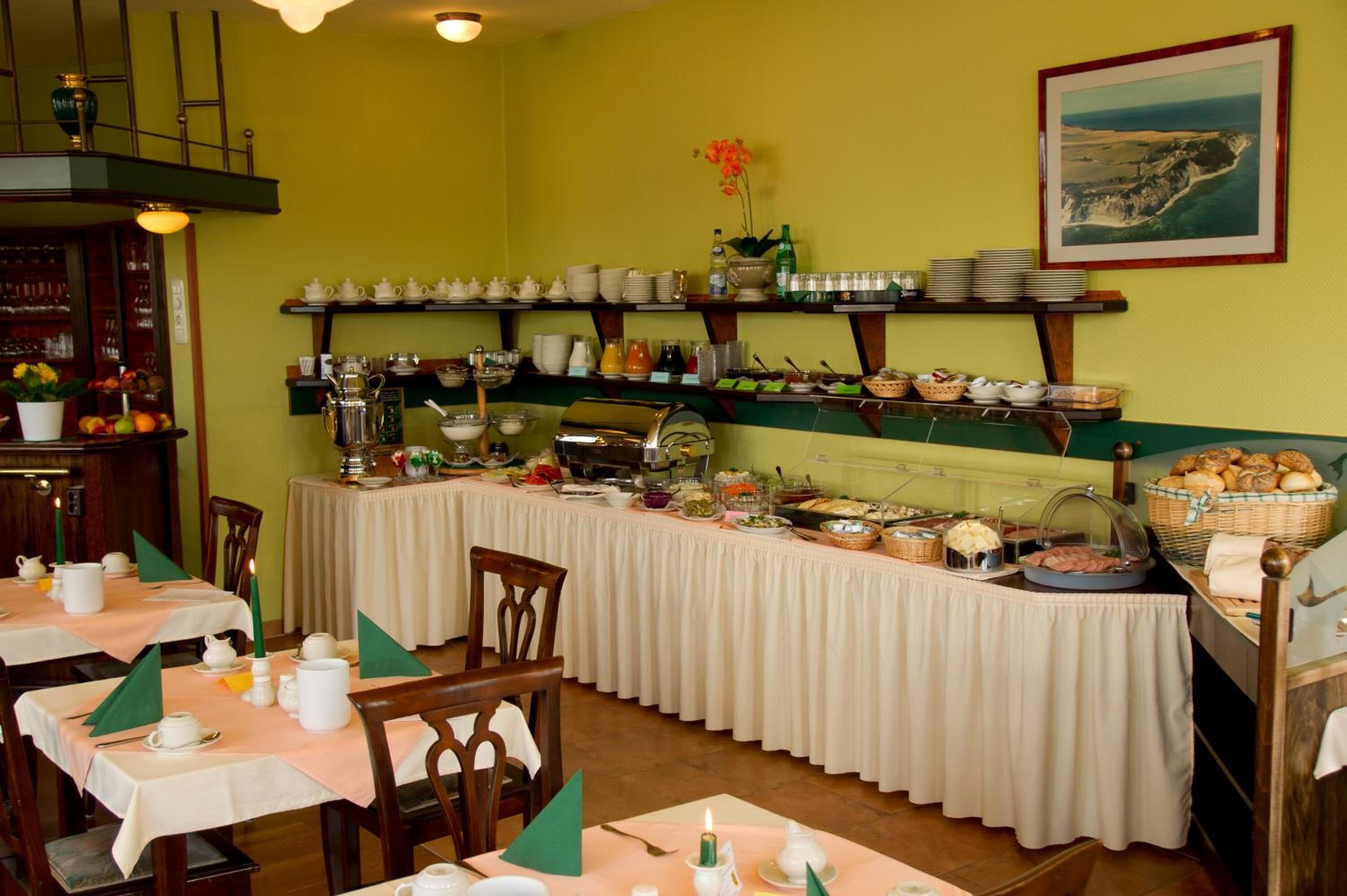 Ein reichhaltiges Buffet mit verschiedenen Speisen, Geschirr und Besteck an Tischen, eine Kaffeestation und ein Wandregal mit Geschirr.