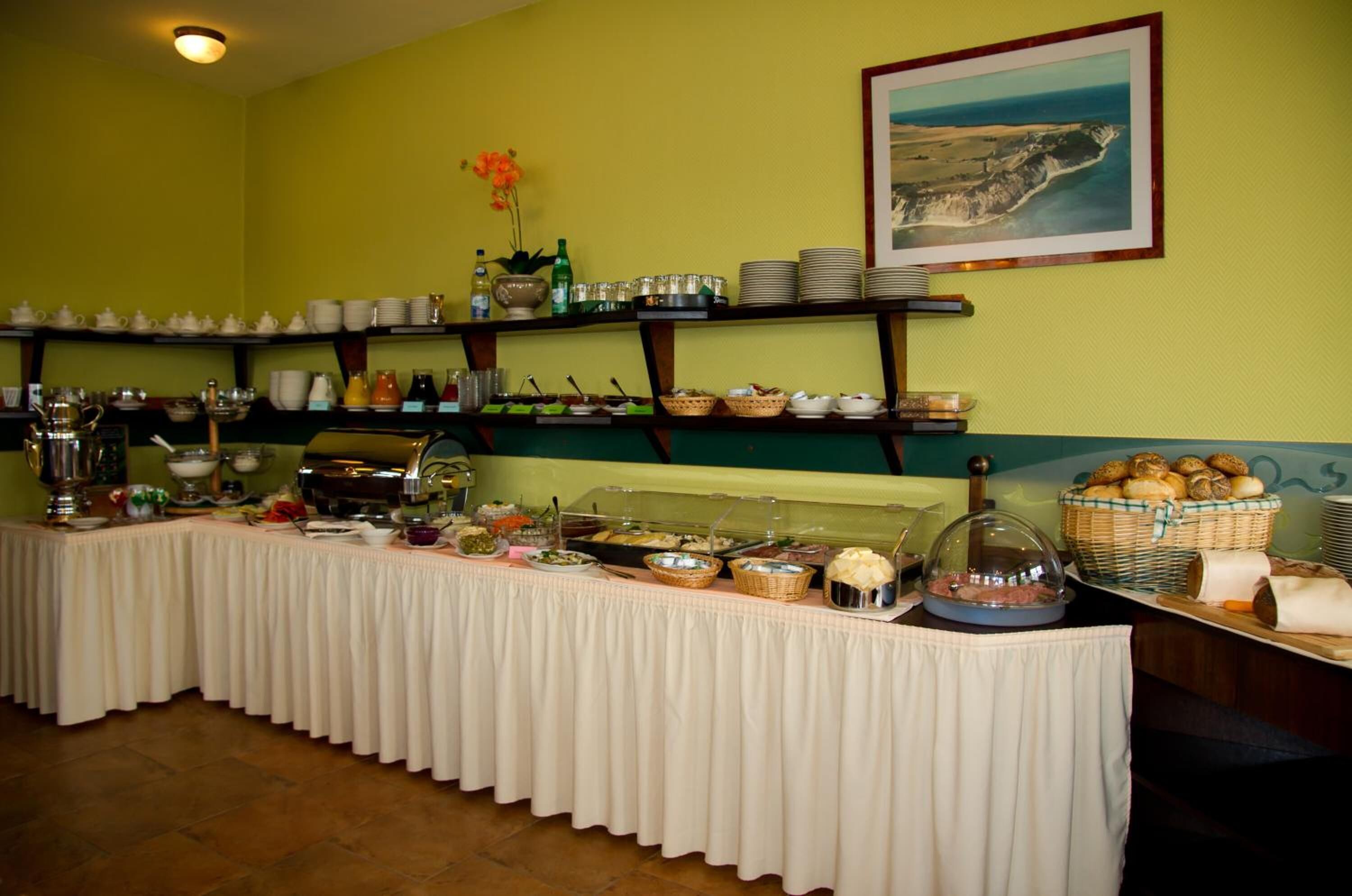 A buffet setup with various food items and utensils on a table, surrounded by shelves with plates and bowls.