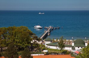 A coastal scene with a pier extending into the sea, a boat docked at the pier, and a building with a green roof in the foreground.