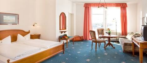 Habitación de hotel con cama doble, escritorio y silla, una mesita con otra silla, televisión y ventana con cortinas.