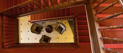 A room with a wooden ladder, a window with a view of a red wall, and a small table with a plant.