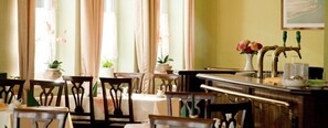 A dining area with wooden chairs and tables, a bar with taps, and a vase with flowers on the counter.