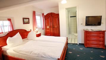 Habitación de hotel con cama doble, armario de madera, televisor y baño con ducha e inodoro.